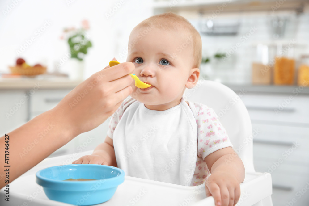 Mother feeding baby with spoon in kitchen Mother feeding baby with spoon in kitchen