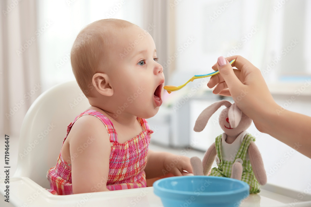 Mother feeding baby with spoon indoors Mother feeding baby with spoon indoors
