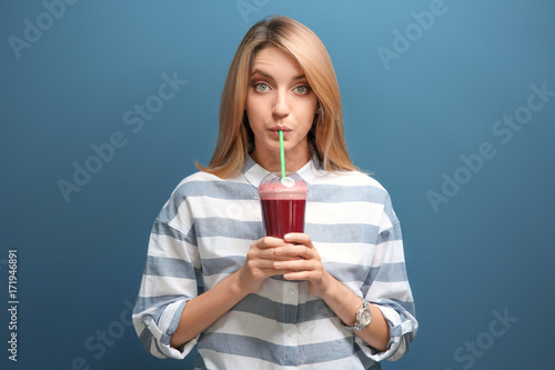 Beautiful young woman with fresh smoothie on color background