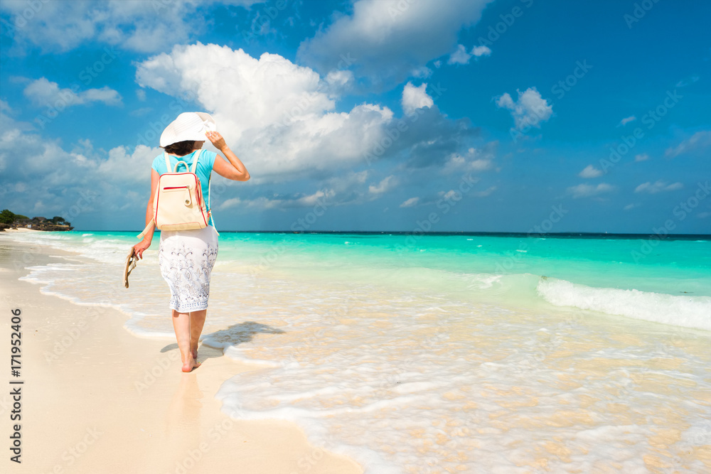 White woman walking along the shore, sand, blue waters of ocean and dark sky White woman walking along the shore, sand, blue waters of ocean and dark sky