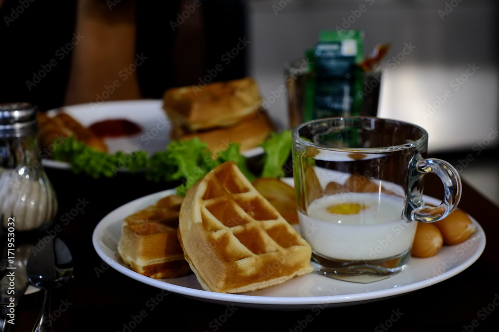 a simple breakfast set consisting of waffles , boiled eggs , sausage ,  vegetables.