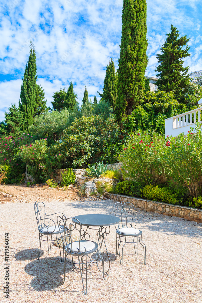 Fototapeta premium Three metal chairs with table on gravel patio in mediterranean garden near Primosten town, Dalmatia, Croatia