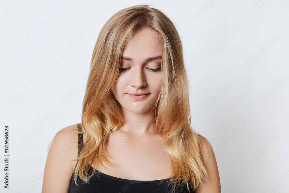 Portrait of young appealing blonde female looks pensively down, wears casual clothes, thinks about relationships or how to solve problem, isolated over white background. People and beauty concept Portrait of young appealing blonde female looks pensively down, wears casual clothes, thinks about relationships or how to solve problem, isolated over white background. People and beauty concept