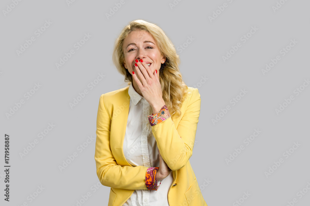 Portrait of cheerful young lady. Happy smiling young woman covering her mouth with hand standing on grey background. Portrait of cheerful young lady. Happy smiling young woman covering her mouth with hand standing on grey background.