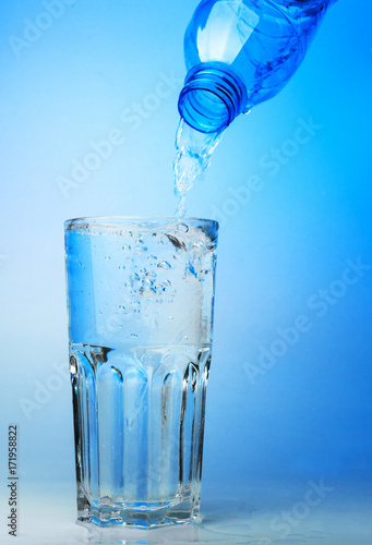 Close up shot : Pour water from plastic bottle in to the glass on blue backgroud