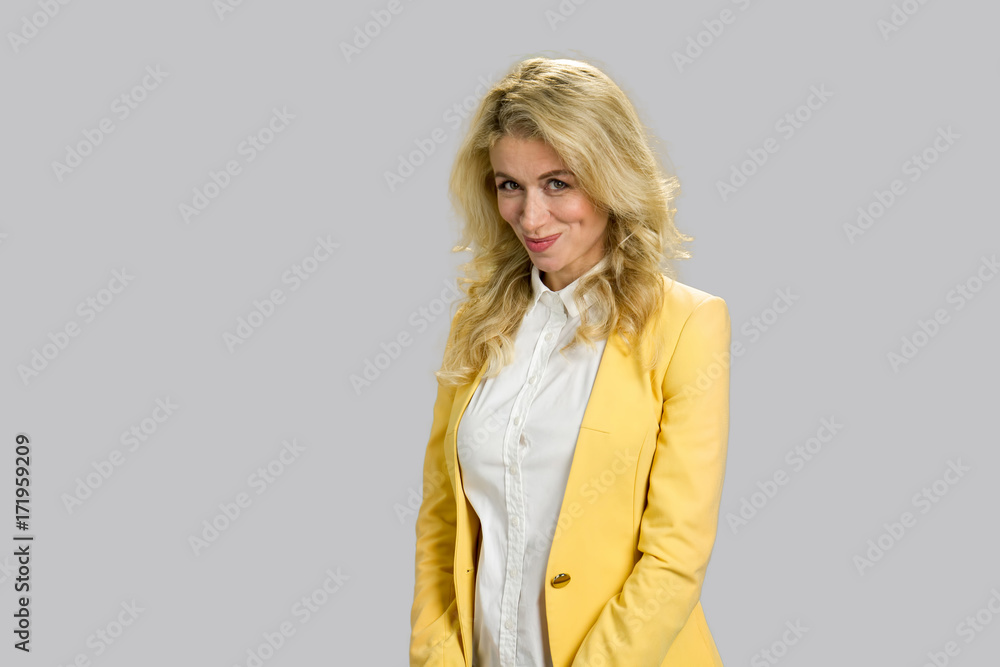 Portrait of positive young woman. Attractive blonde lady in yellow jacket looking embarrassed standing on grey background close up. Portrait of positive young woman. Attractive blonde lady in yellow jacket looking embarrassed standing on grey background close up.