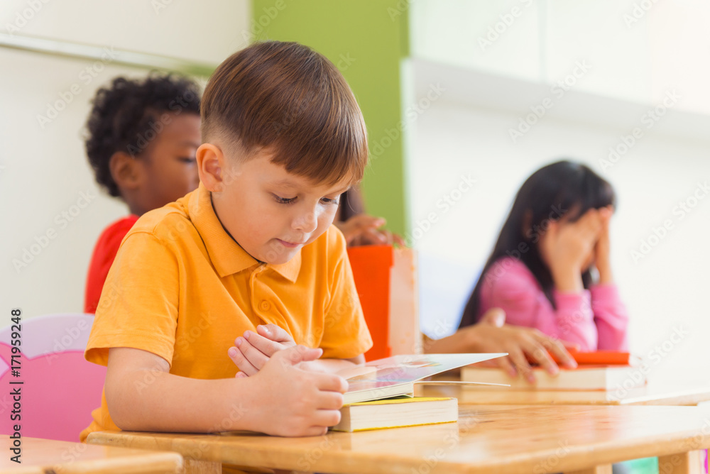 Row of multiethnic elementary students reading book in classroom. Vintage effect style pictures. Row of multiethnic elementary students reading book in classroom. Vintage effect style pictures.