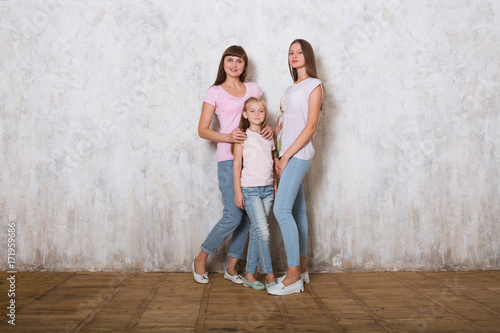 beautiful mom with two her daughters posing against gray wall, minimalist street fashion style, family same look.