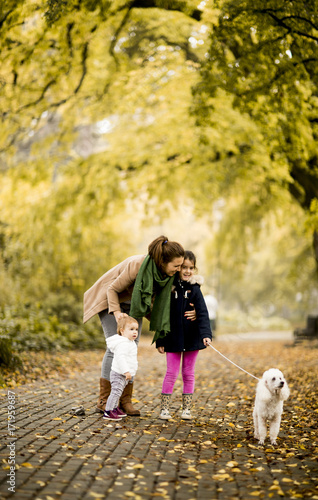 Mother and two girls walking with a dog in the autumn park