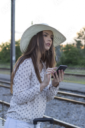 Young beautiful girl at train station with hat on her head and with mobile phone on hand