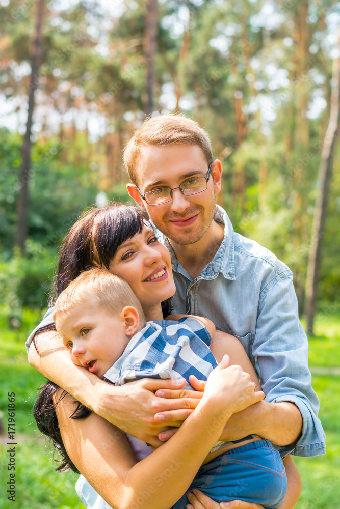 Fototapeta premium Dad hugs mom who holds the child in her arms. Happy family - Mom, Dad and child- for a walk in the park.