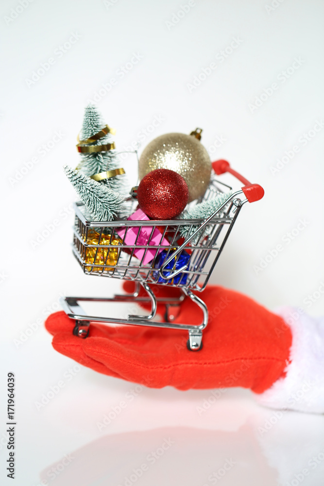 Christmas expenses. Expenses for New Year's . Trolley from a supermarket with a Christmas tree, Christmas ball, gifts at the hands of Santa Claus wearing red gloves 