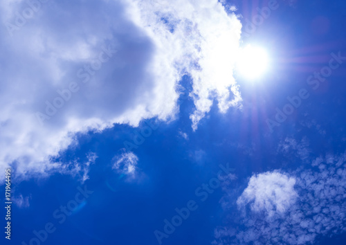 White fluffy clouds in the bright blue sky with light from the Sun