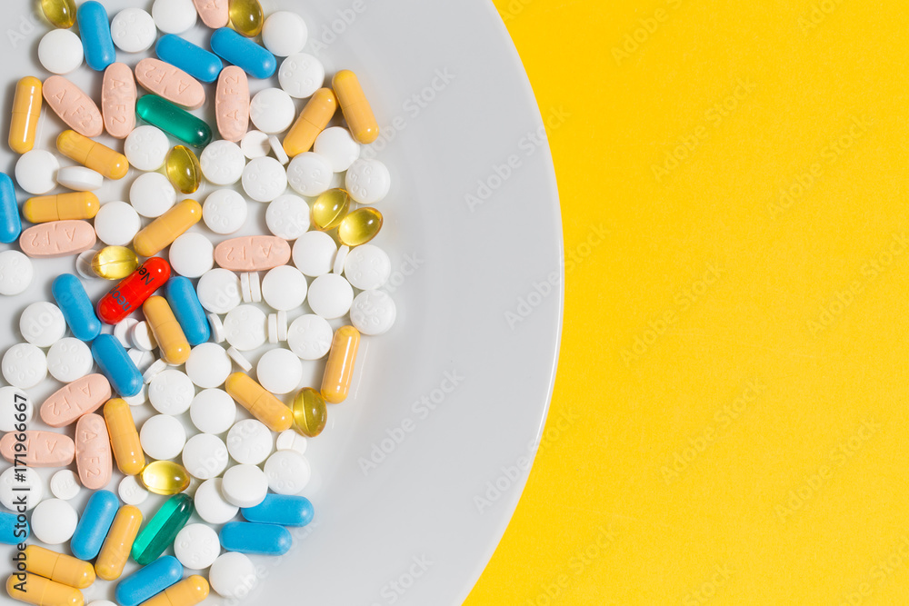 Obraz premium Many pills on a plate isolated on yellow background