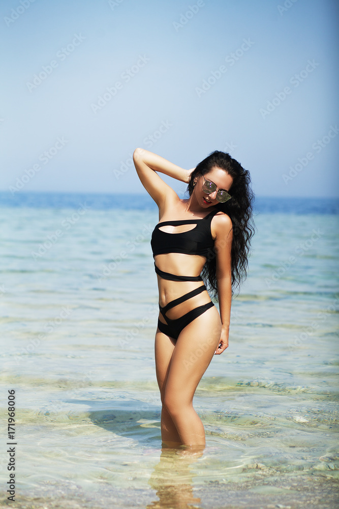 Happy woman with long hair and healthy glowing skin relaxing on a beach in black bikini. Happy woman with long hair and healthy glowing skin relaxing on a beach in black bikini.