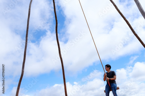 Thai male was playing wooden the swings at Khao Kho, Phetchabun, Thailand with nice cloudy blue sky