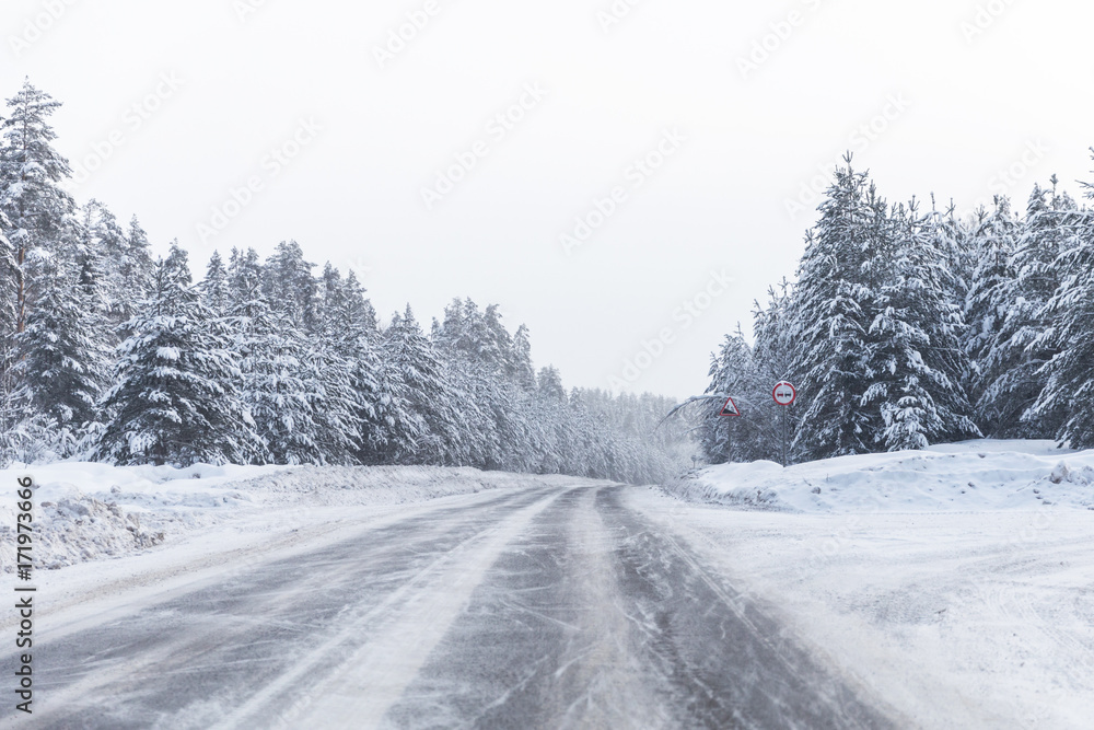 Obraz premium winter road with ice on the asphalt, trees under snow during the winter frost