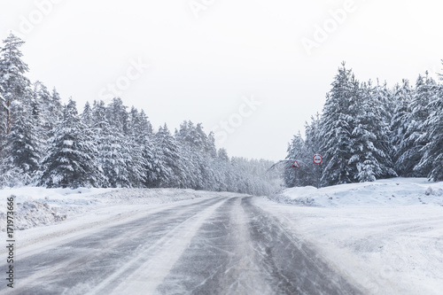 winter road with ice on the asphalt, trees under snow during the winter frost
