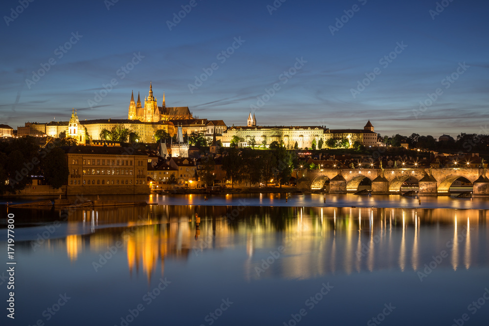 View of the lit Prague (Hradcany) Castle, Charles Bridge (Karluv most) and their reflections on the Vltava River in Prague, Czech Republic, in the evening.