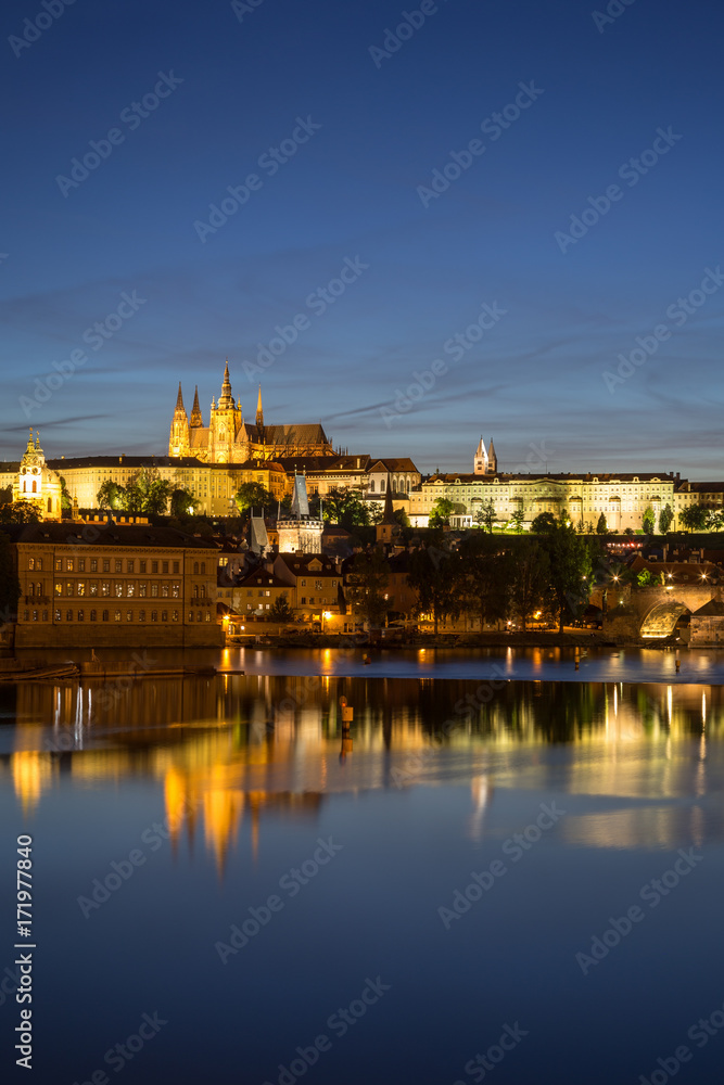 View of the lit Prague (Hradcany) Castle, Charles Bridge (Karluv most) and their reflections on the Vltava River in Prague, Czech Republic, in the evening.