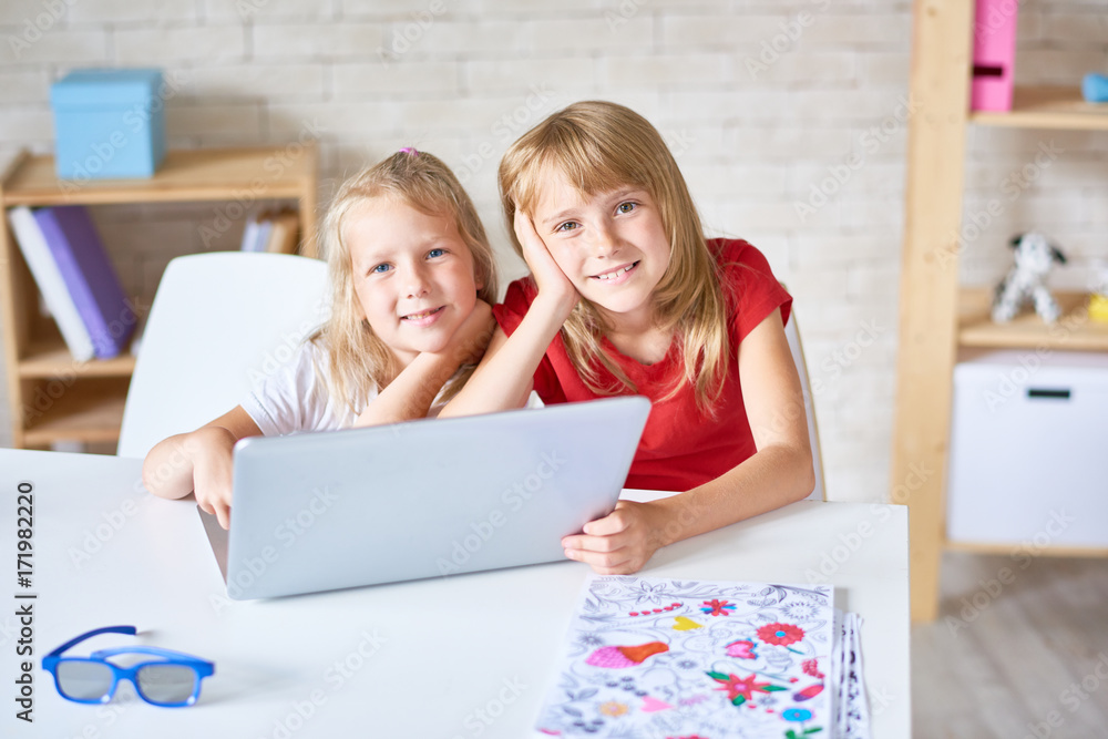 Group portrait of cheerful little sisters posing for photography with toothy smiles while watching their favorite cartoon on laptop, interior of cozy bedroom on background Group portrait of cheerful little sisters posing for photography with toothy smiles while watching their favorite cartoon on laptop, interior of cozy bedroom on background