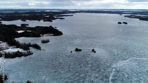 HD Aerial view from frozen lake, islands, shoreline and forests on winter spring cloudy day. Drone flying forward camera turning down at the end of the clip. Kangasala. Finland. Scandinavia photo