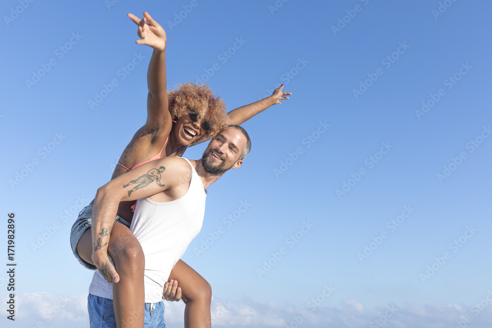 Couple piggy back on the beach in the summer Couple piggy back on the beach in the summer