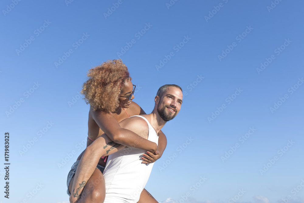 Couple piggy back on the beach in the summer Couple piggy back on the beach in the summer