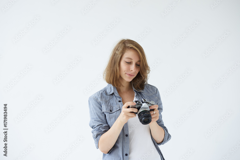 Fototapeta premium Attractive professional young female photographer viewing images on her digital camera while shooting in studio, having pleased look. People, photography, hobby, profession and occupation concept