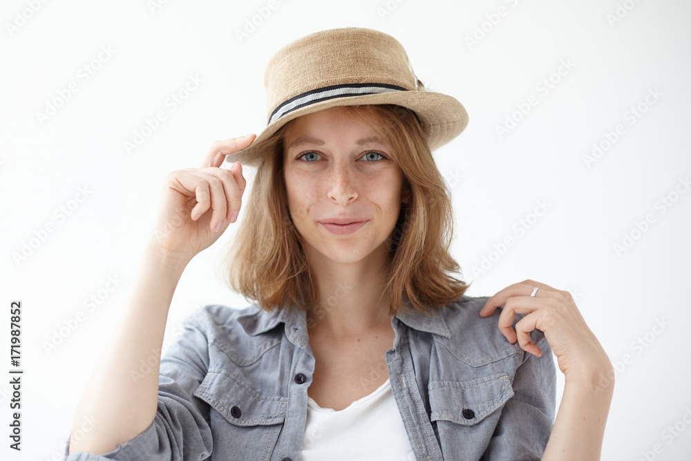 Headshot of stunning fashionable young female wearing summer straw hat in studio while choosing clothes for journey on vacations. Stylish girl model smiling joyfully posing in trendy round headwear Headshot of stunning fashionable young female wearing summer straw hat in studio while choosing clothes for journey on vacations. Stylish girl model smiling joyfully posing in trendy round headwear