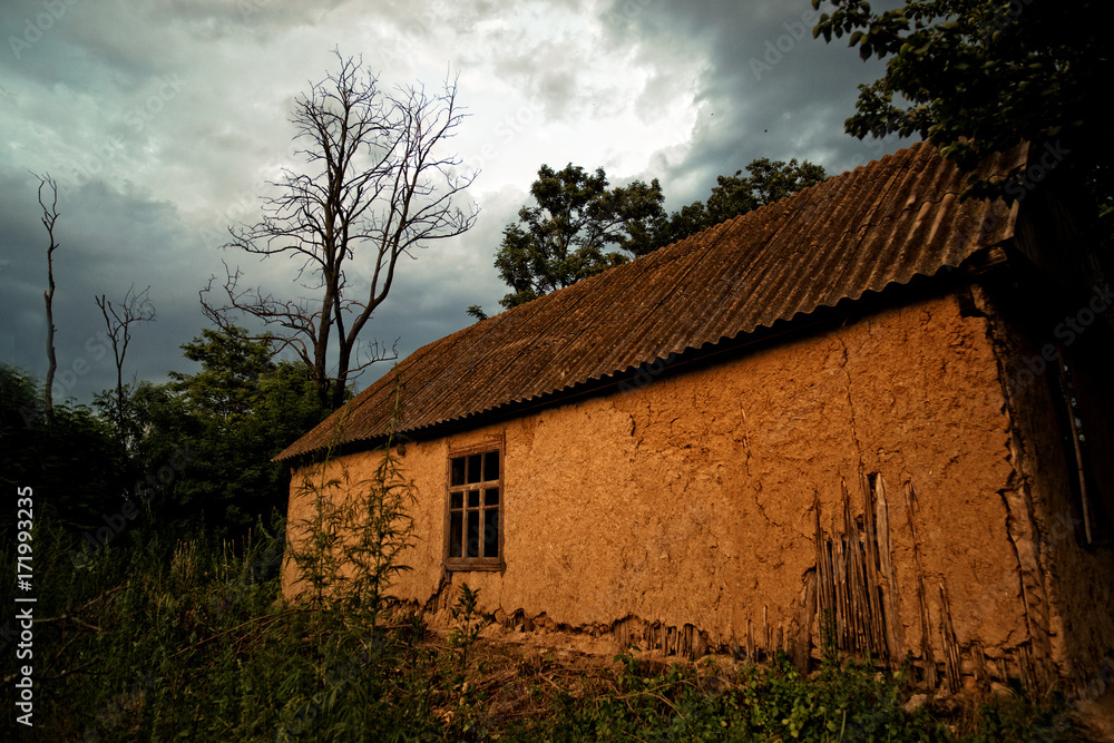 Fototapeta premium Old Ukrainian village house (mud hut) at sunset on the edge of the forest