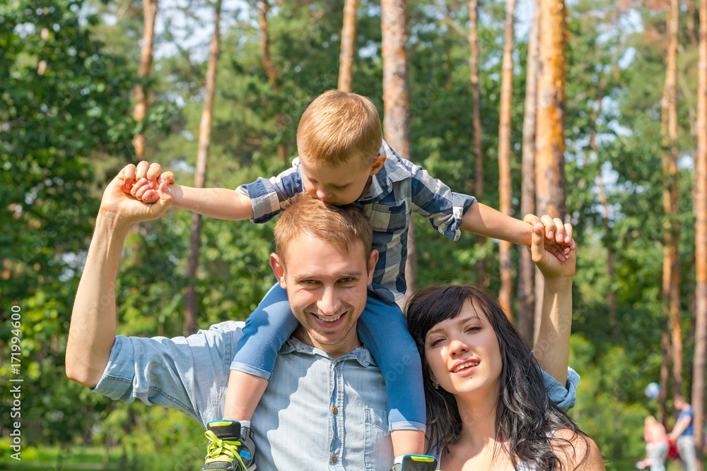 Fototapeta premium Daddy carries his son on his shoulders, mom laughs next to them.