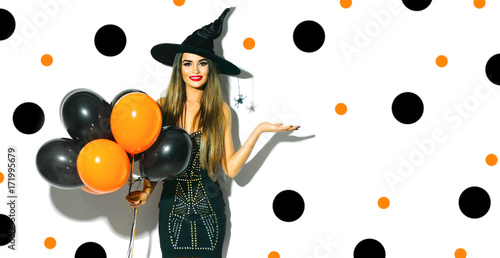 Halloween party girl. Sexy witch holding black and orange air balloons. Beautiful young woman in witches hat and costume