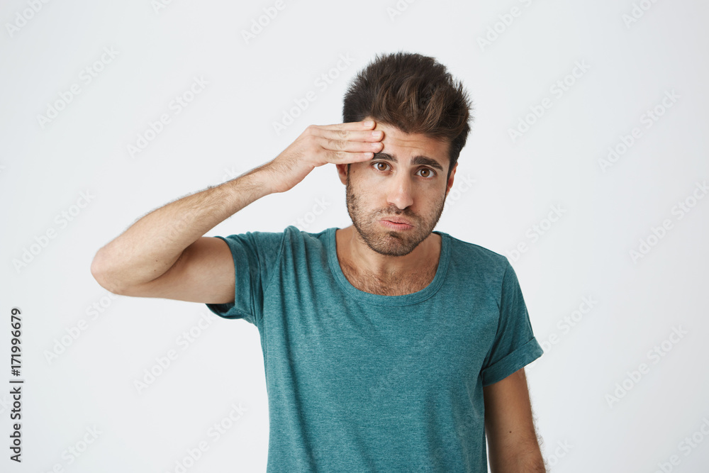 Portrait of young tired caucasian guy wearing blue tshirt wiping his forehead with hand being tired after complex training. Body language. Portrait of young tired caucasian guy wearing blue tshirt wiping his forehead with hand being tired after complex training. Body language.