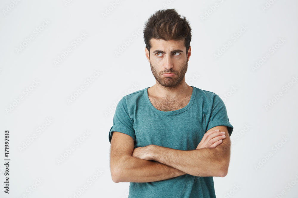 Close up isolated portrait of unhappy hispanic guy in trendy clothes and haircut, looking away, pursuing lips expressing insult and dissatisfaction. Human emotions. Copy space. Close up isolated portrait of unhappy hispanic guy in trendy clothes and haircut, looking away, pursuing lips expressing insult and dissatisfaction. Human emotions. Copy space.