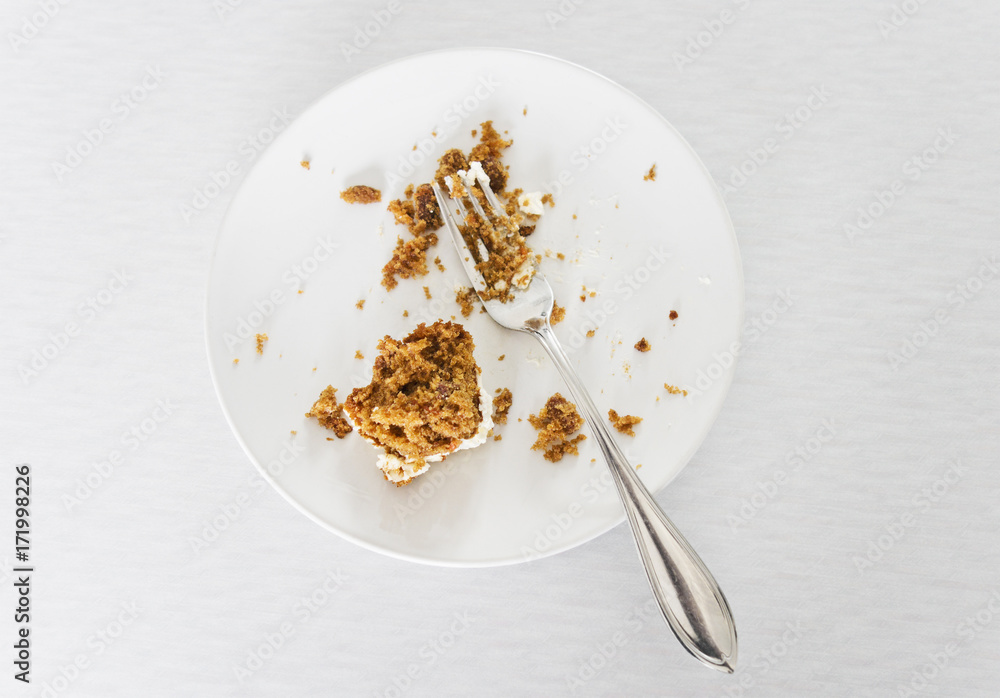 Carrot cake leftovers with fork on a dessert plate on a light background