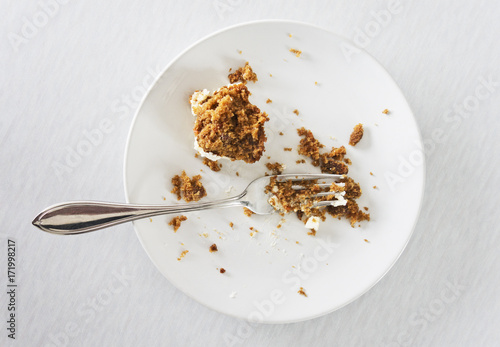 Deset late with carrot cake remains and fork on a light coloured background.