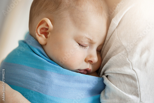 Close up portrait of innocent little child, sleeping on mother hands in blue baby sling. Quite and relaxing scene. Family, lifestyle concept.