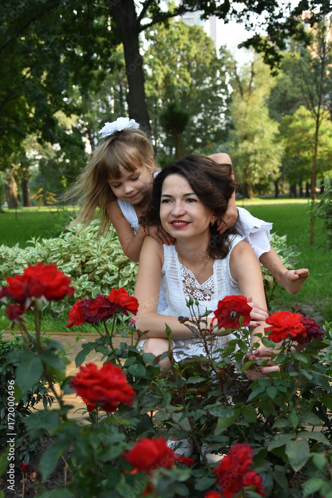  Happy family, girl with blond hair with mother between red roses