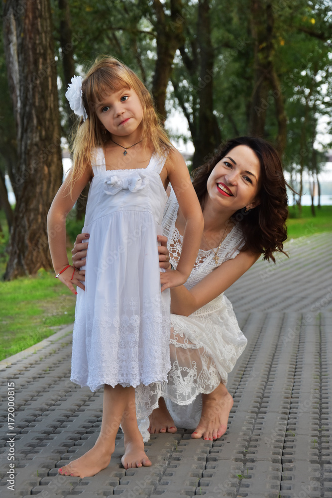 Mom and daughter in white dresses are playing on the path in the park Mom and daughter in white dresses are playing on the path in the park