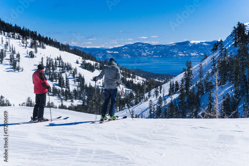 Two middle aged men on skis look out over the lake tahoe mountains
