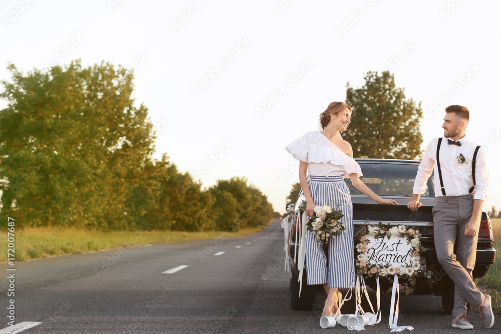 Happy wedding couple near decorated car outdoors Happy wedding couple near decorated car outdoors