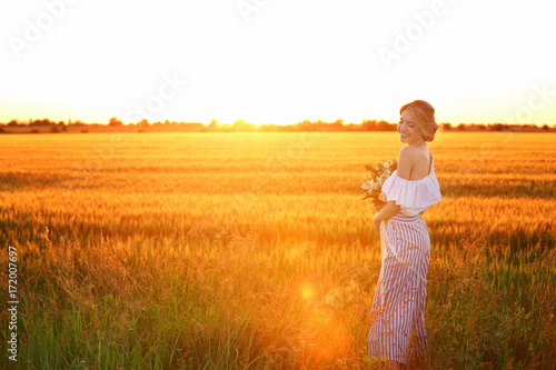 Beautiful young bride with bouquet in field at sunset
