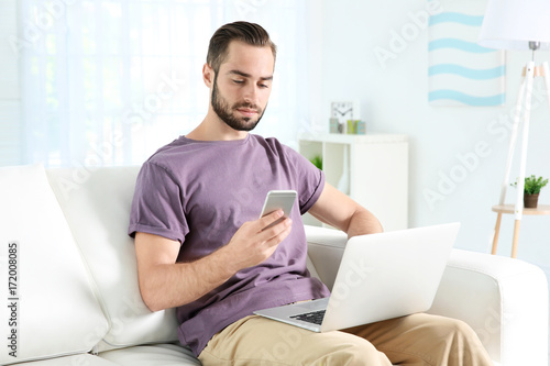 Young man searching information using laptop and phone at home