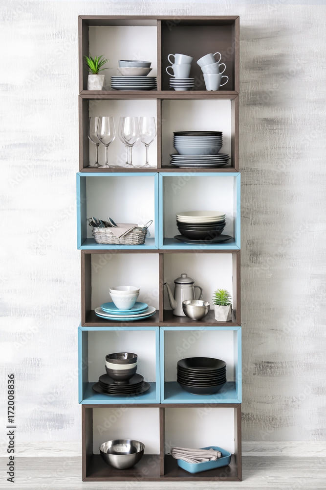 Storage stand with ceramic dishware on light wall background Storage stand with ceramic dishware on light wall background