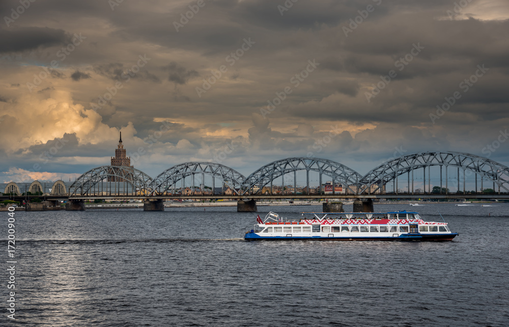 Sightseeing cruise boat on the river Daugava in Latvian capital Riga. Railway bridge in the background.