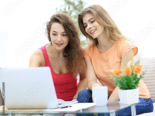 two student girls looking at laptop screen while sitting on the couch.