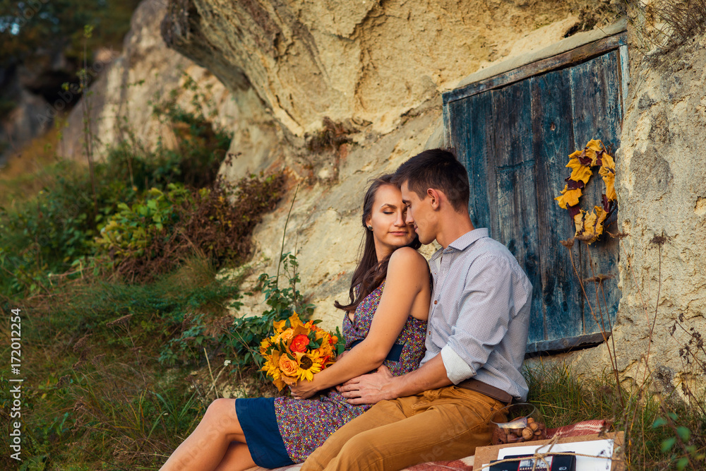 Φωτογραφία Sensual lovely couple sitting on the plaid near the rock with caves and blue wooden door