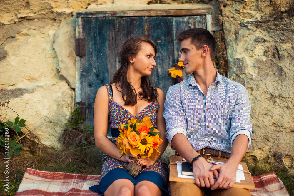 Φωτογραφία Sensual lovely couple sitting on the plaid near the rock with caves and blue wooden door