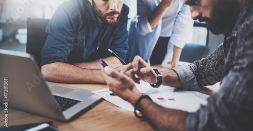 Teamwork concept.Group of three coworkers working together in modern coworking studio.Bearded man using smartphone showing new startup project.Horizontal cropp.Blurred background.